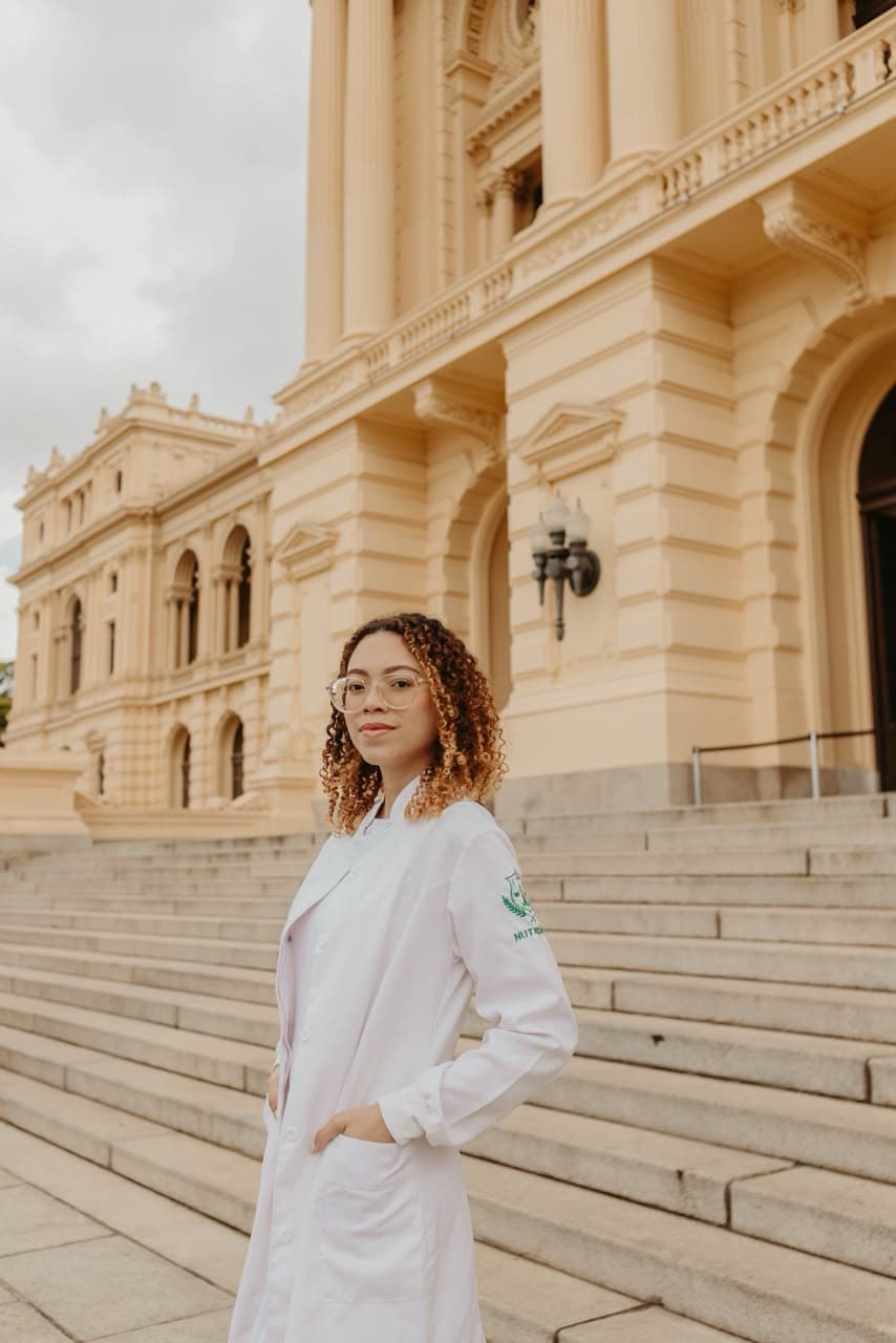 Larissa Genari, nutricionista, de jaleco em frente a um edifício histórico