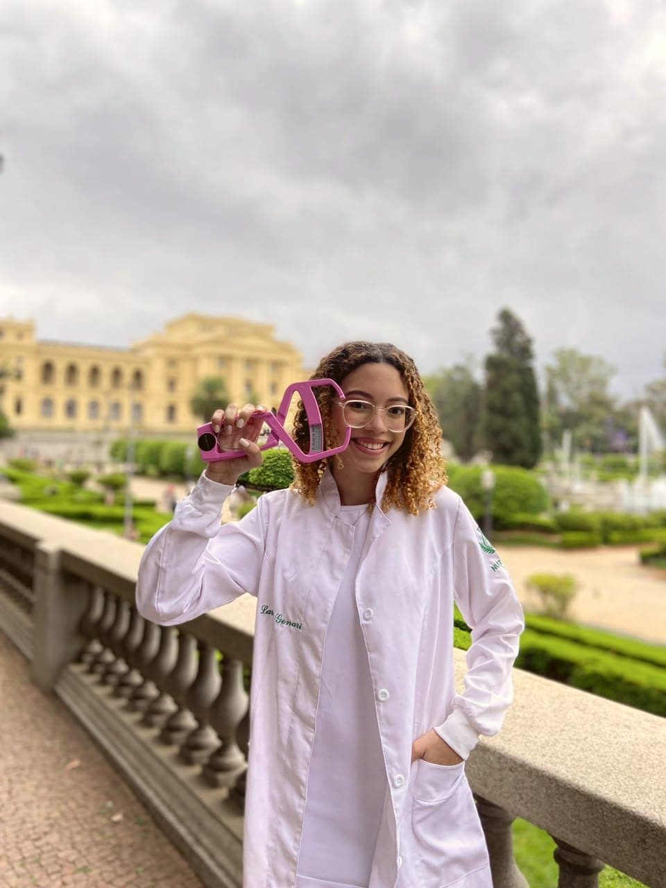 Larissa Genari sorrindo, de jaleco, segurando um adipômetro